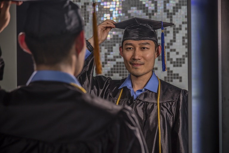 man looking at himself in the mirror while wearing cap and gown