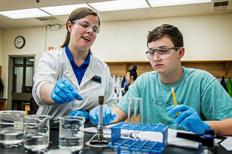Student watches a instructor heats a test tube up over a bunsen burner.