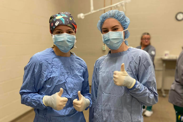 two vet tech students in scrubs giving thumbs up